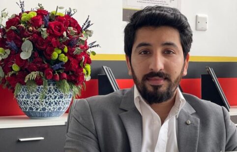 Man sitting with floral arrangement behind.